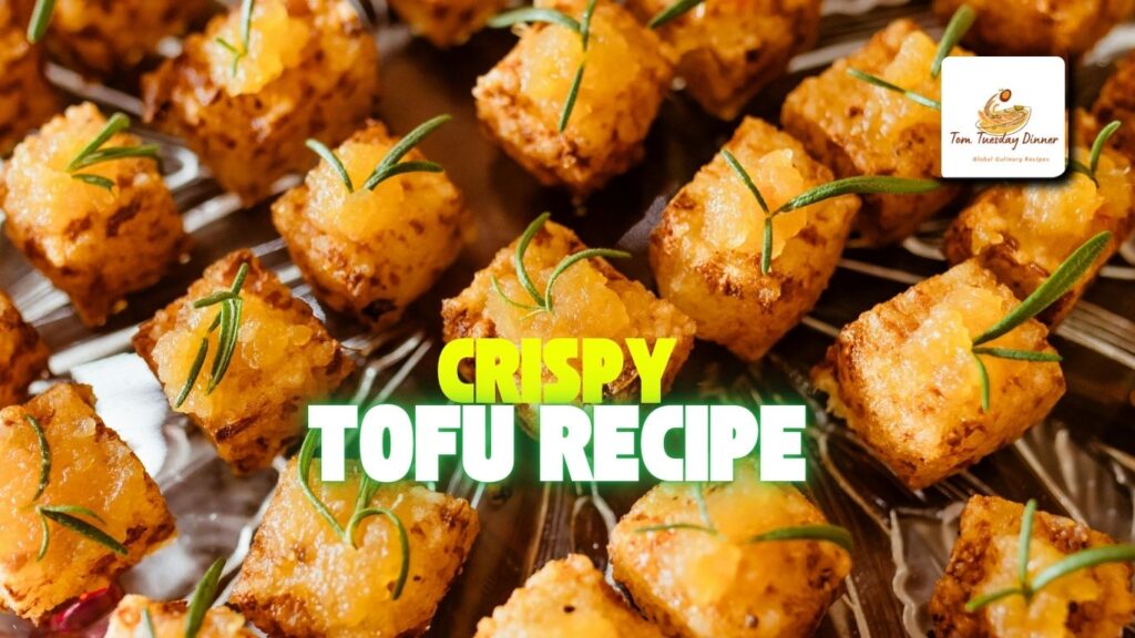 Golden crispy tofu cubes served on a white plate with a sprinkle of sesame seeds and fresh herbs, ready to eat.