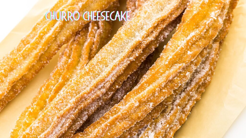 Close-up of crispy, sugar-coated churros arranged on a piece of parchment paper with the text "Churro Cheesecake" above.