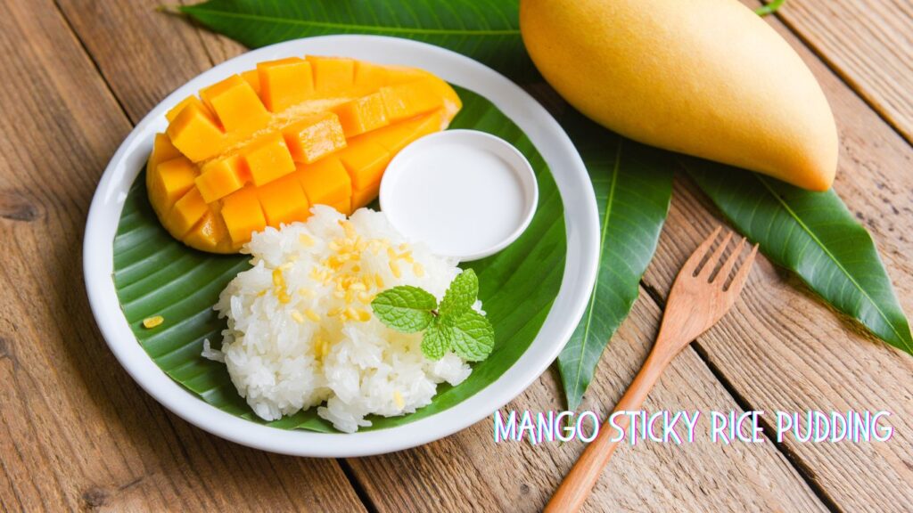 A plate of mango sticky rice pudding featuring sliced ripe mango, sticky rice topped with mung beans and mint leaves, served with coconut milk on a banana leaf, with a whole mango and wooden fork on the side.