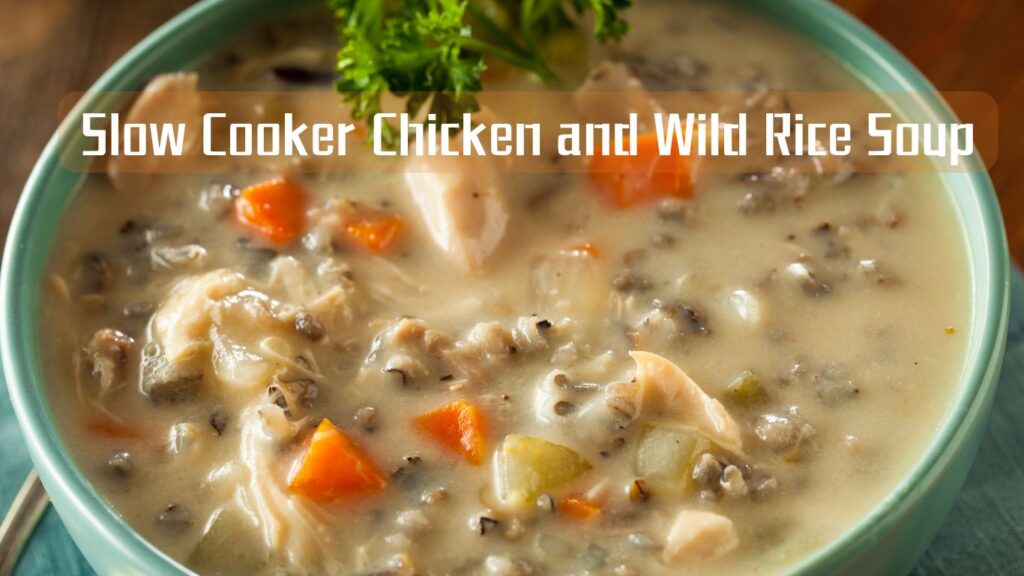 A close-up image of a creamy slow cooker chicken and wild rice soup garnished with parsley, featuring chunks of chicken, diced carrots, and wild rice in a thick broth.