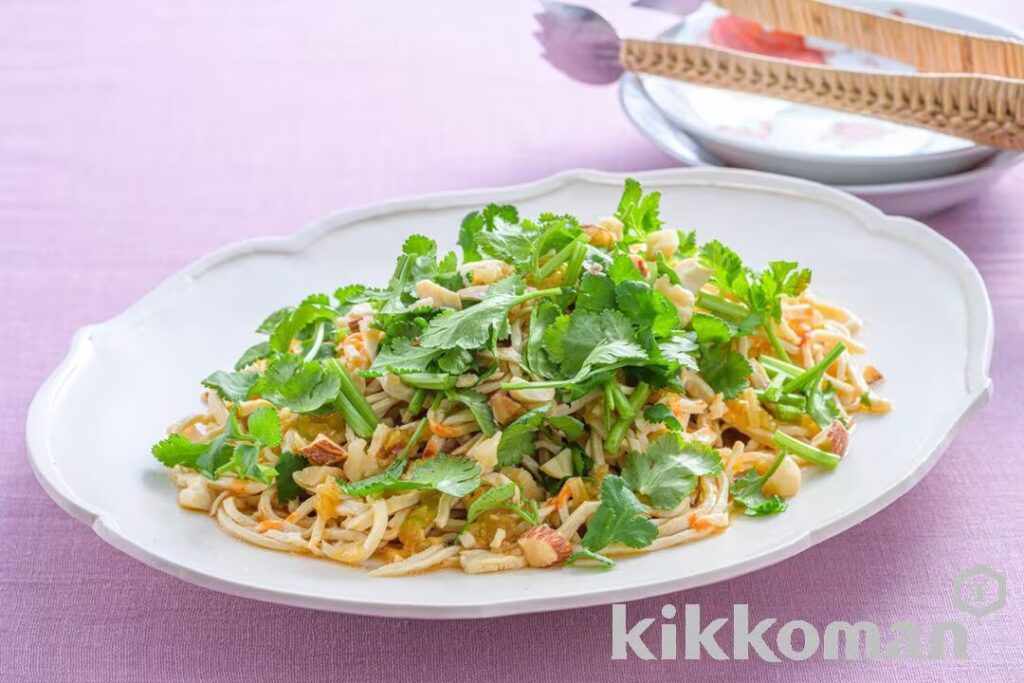 A plate of Asian-style salad with fresh herbs and peanuts on a purple tablecloth.