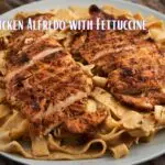 A plate of Chicken Alfredo with Fettuccine featuring two grilled chicken breasts on top of creamy fettuccine pasta.