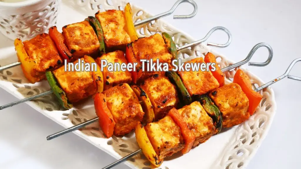 A platter of Indian Paneer Tikka skewers with chunks of paneer, bell peppers, and zucchini grilled and served on metal skewers.