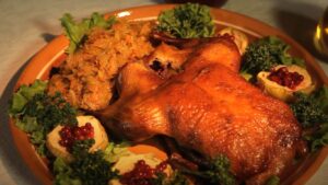 A roasted turkey on a serving platter garnished with green lettuce and broccoli, accompanied by side dishes that include pomegranate seeds.