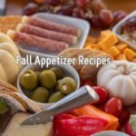 A spread of various appetizers including cheeses, meats, fruits, and olives with small pumpkins and autumn leaves, labeled “Fall Appetizer Recipes.”