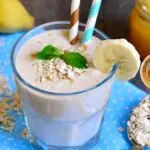 A glass of banana oat smoothie garnished with mint leaves, accompanied by ingredients like bananas, oats, honey, and soy milk.