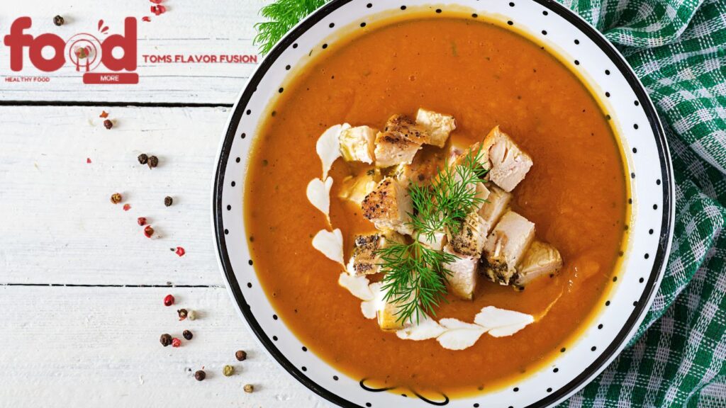 A bowl of creamy pumpkin soup topped with grilled chicken pieces, fresh dill, and a drizzle of cream, served in a white bowl with black polka dots.