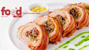 Sliced bacon-wrapped meatloaf stuffed with mushrooms and vegetables on a white plate with mustard sauce and green sauce garnish.