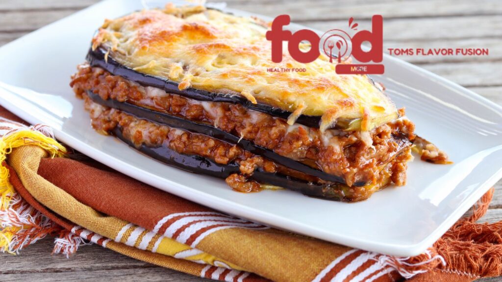 Layered eggplant casserole with minced meat and melted cheese on a white plate, topped with a golden, bubbly cheese crust.