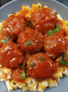 A plate of pasta topped with meatballs in tomato sauce, garnished with fresh herbs.