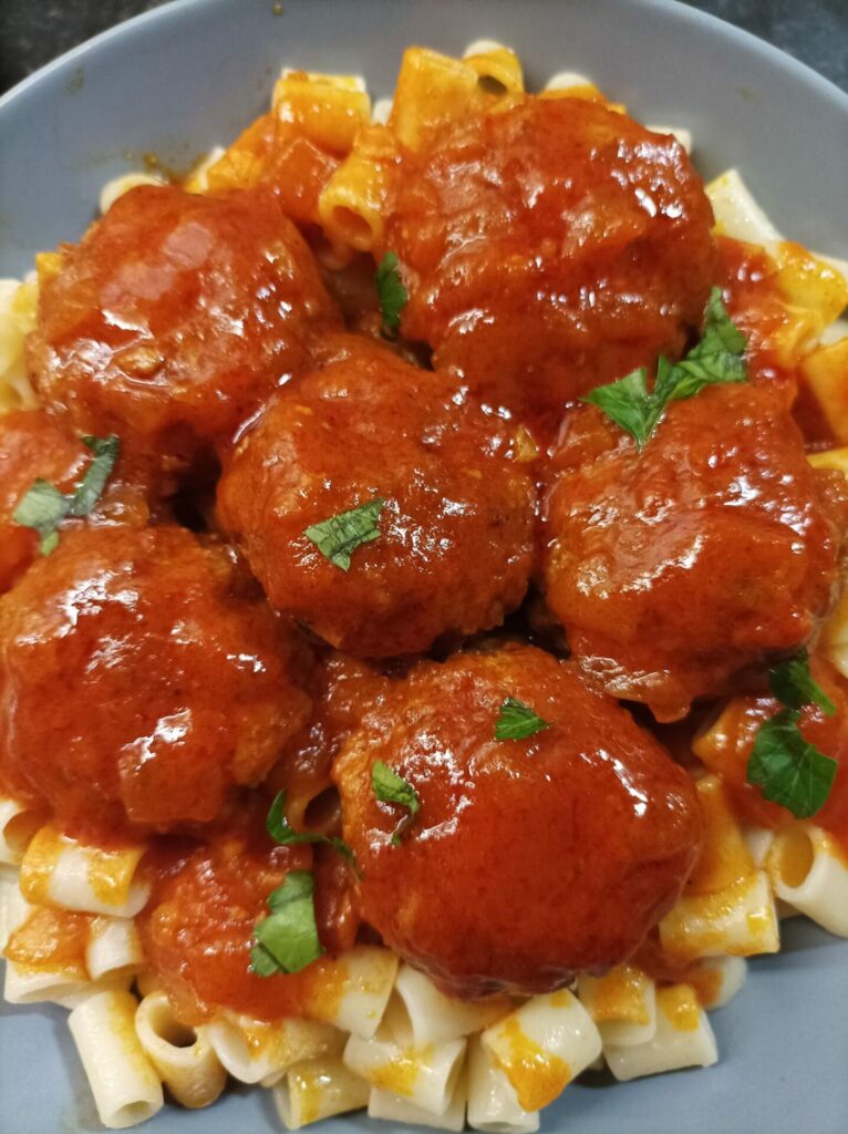 A plate of pasta topped with meatballs in tomato sauce, garnished with fresh herbs.