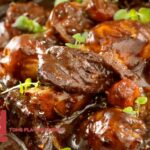 Close-up of a rich and hearty beef stew with tender beef chunks, carrots, and a glossy, savory broth garnished with fresh herbs.