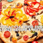 A colorful focaccia bread topped with sun-dried tomatoes, yellow and red bell peppers, and various herbs, displayed on a wooden surface with a knife and scattered peppercorns. The text "Easy Focaccia with Sun-Dried Tomatoes Recipe & Nutrition" is prominently displayed.