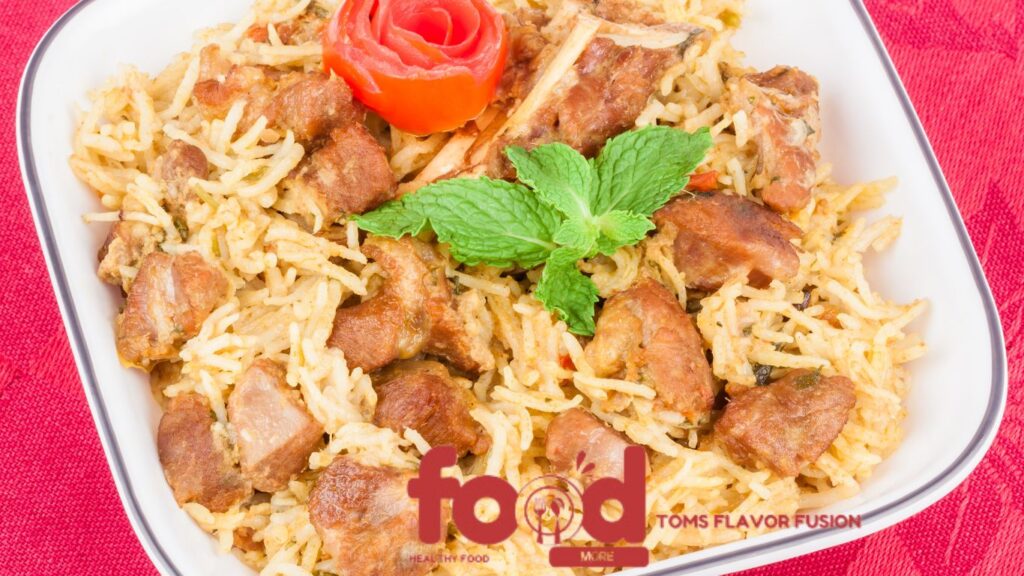 A bowl of biryani with pieces of meat, garnished with a mint leaf and a tomato rose, placed on a red cloth.