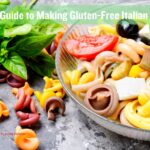 A colorful bowl of gluten-free Italian pasta salad featuring vibrant tri-color pasta, fresh basil, olives, tomatoes, bell peppers, and cheese cubes, placed next to a bundle of fresh basil leaves on a textured gray surface.