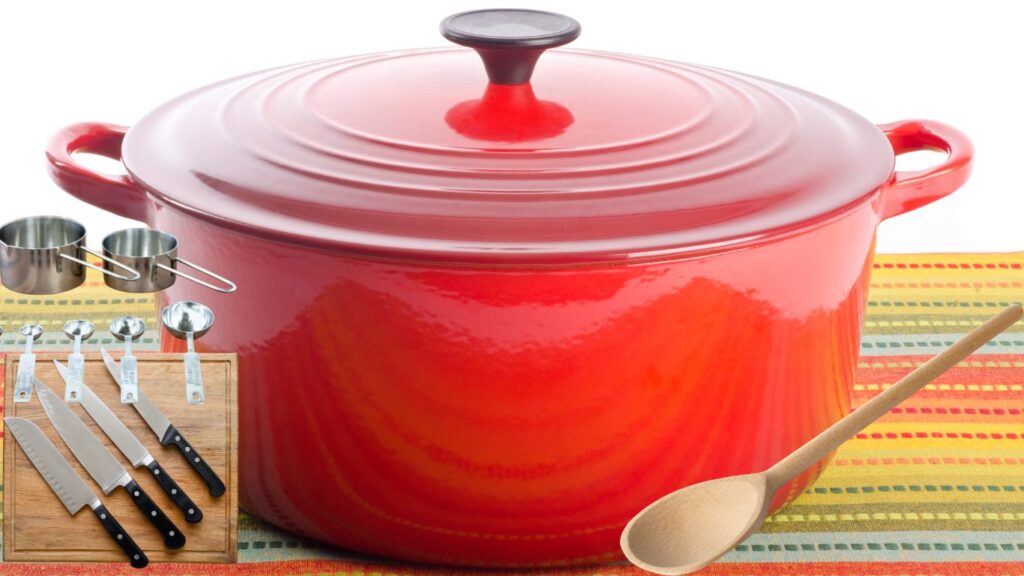 A large red Dutch oven with a lid, accompanied by a wooden spoon, measuring cups, measuring spoons, and a set of kitchen knives.