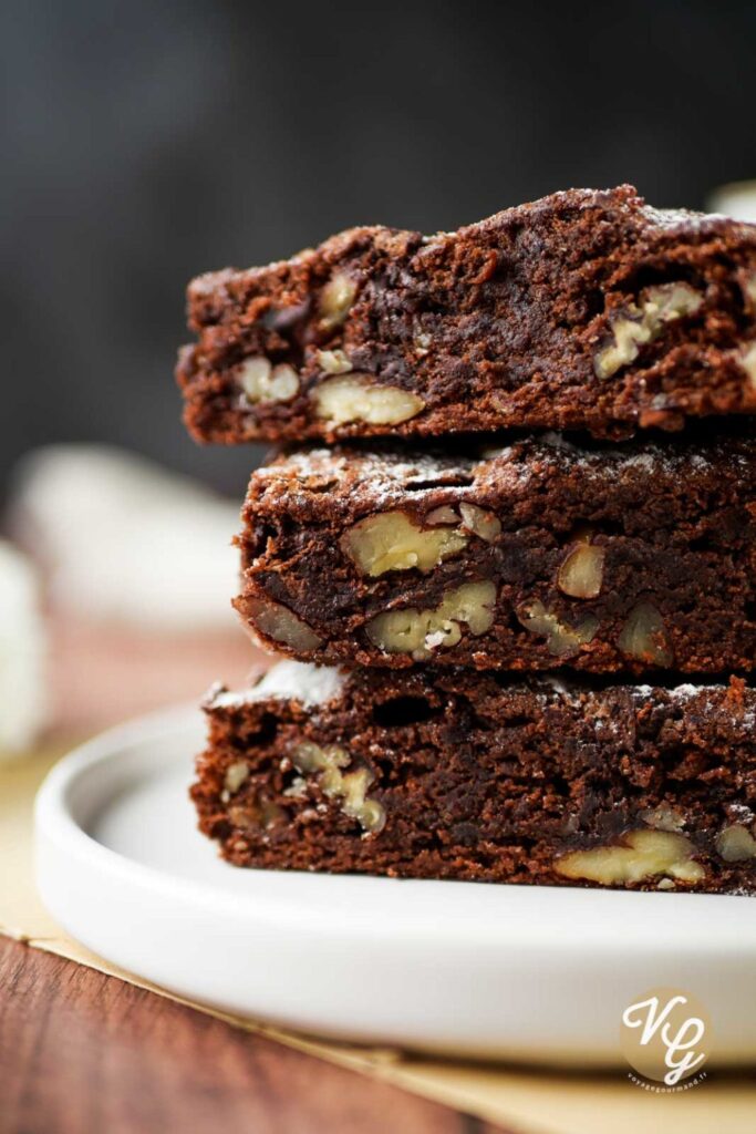 A close-up of three stacked chocolate brownies with visible chunks of walnuts, placed on a white plate.