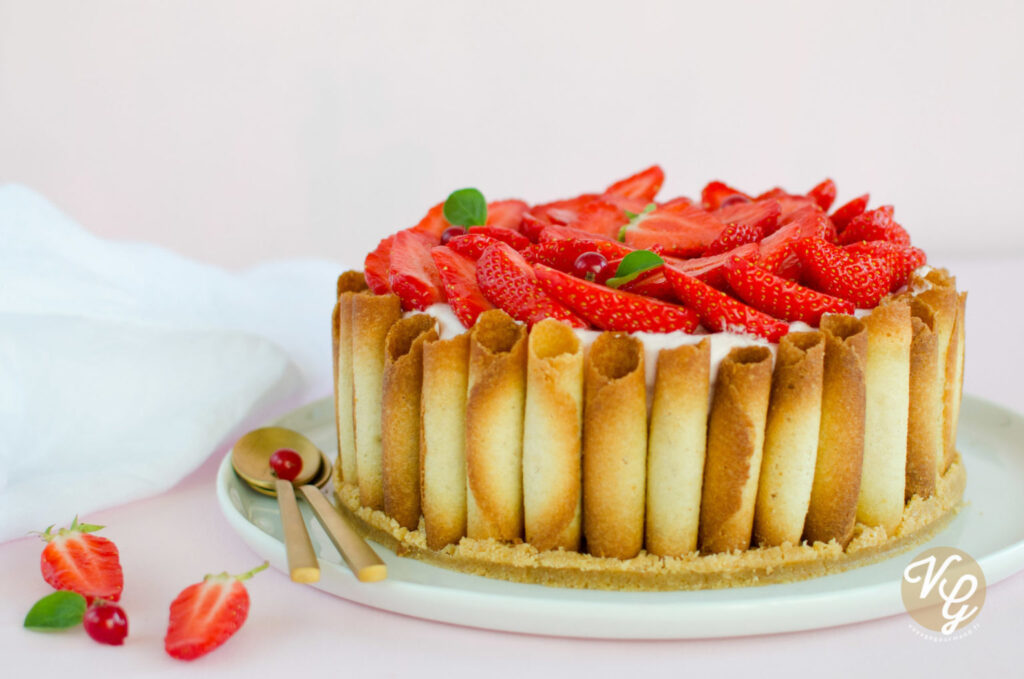 A beautifully decorated cake with a border of rolled wafer cookies and topped with fresh sliced strawberries and small green leaves.