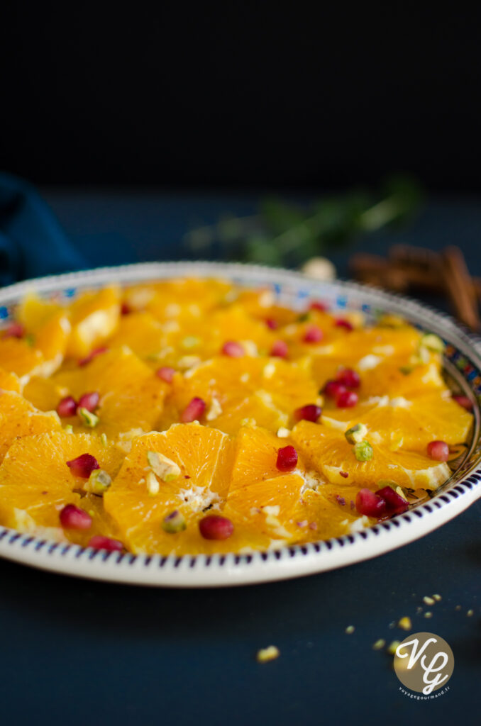 A close-up of a plate of sliced oranges garnished with pomegranate seeds and chopped pistachios.