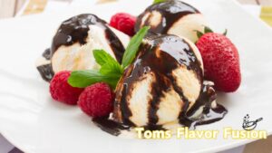 Three scoops of vanilla ice cream topped with chocolate sauce, garnished with fresh raspberries, strawberries, and mint leaves on a white plate. The text "Toms Flavor Fusion" is displayed in yellow at the bottom right corner.