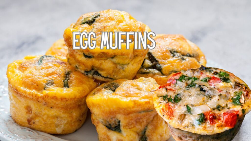 A close-up of several egg muffins stacked on a plate. The muffins are golden brown with visible green and red vegetable pieces. The text "EGG MUFFINS" is overlaid on the image.