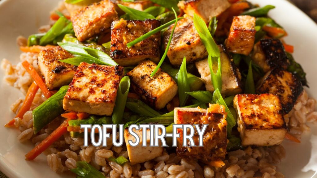 A close-up of a tofu stir-fry dish featuring grilled tofu cubes, green beans, carrots, and green onions served over a bed of brown rice.