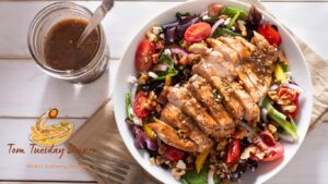 Fresh Caesar Salad with grilled chicken, vibrant greens, cherry tomatoes, walnuts, and a jar of homemade dressing on a wooden table.