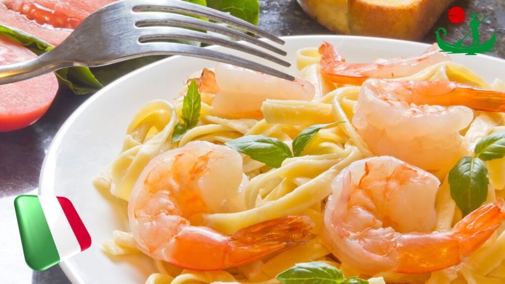 A close-up of a plate of pasta with shrimp and basil leaves, with a fork poised above the dish. In the background, there are slices of tomato and a piece of bread. An Italian flag icon is present in the bottom left corner, and a green gondola logo with a red sun is in the top right corner.