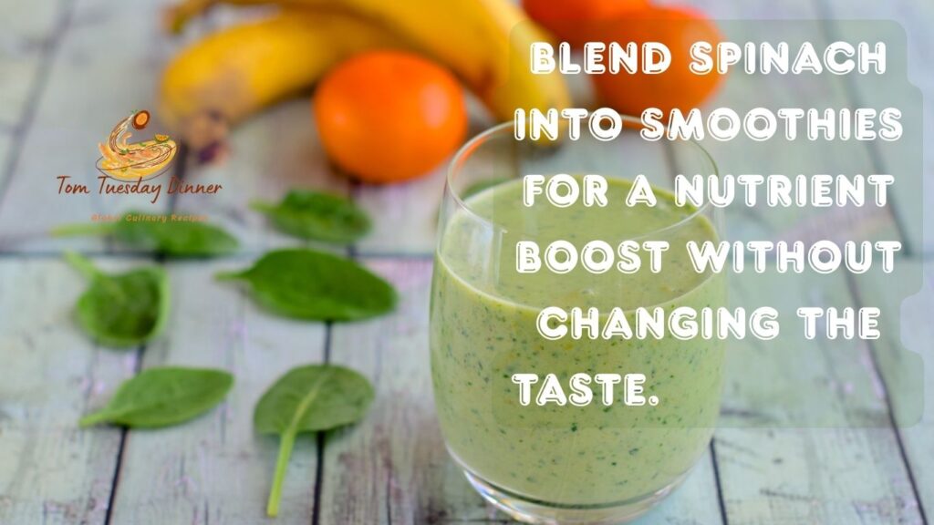 A glass of green smoothie with spinach leaves, bananas, and oranges in the background. Text overlay reads: "Blend spinach into smoothies for a nutrient boost without changing the taste."