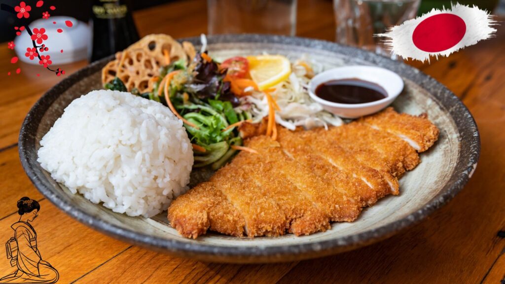 A plate of Japanese cuisine featuring rice, breaded and fried meat cutlet, assorted vegetables, and a small dish of sauce. The plate is garnished with a slice of lemon and lotus root slices. The background includes a Japanese flag and cherry blossom illustration.