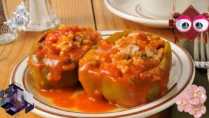 Two stuffed green bell peppers topped with tomato sauce on a white plate with a brown rim, placed on a wooden table. Decorative elements including flowers, geometric shapes, and a cartoonish face with large eyes are added around the image.