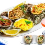 A plate of assorted baked oysters with lemon wedges and a cocktail.