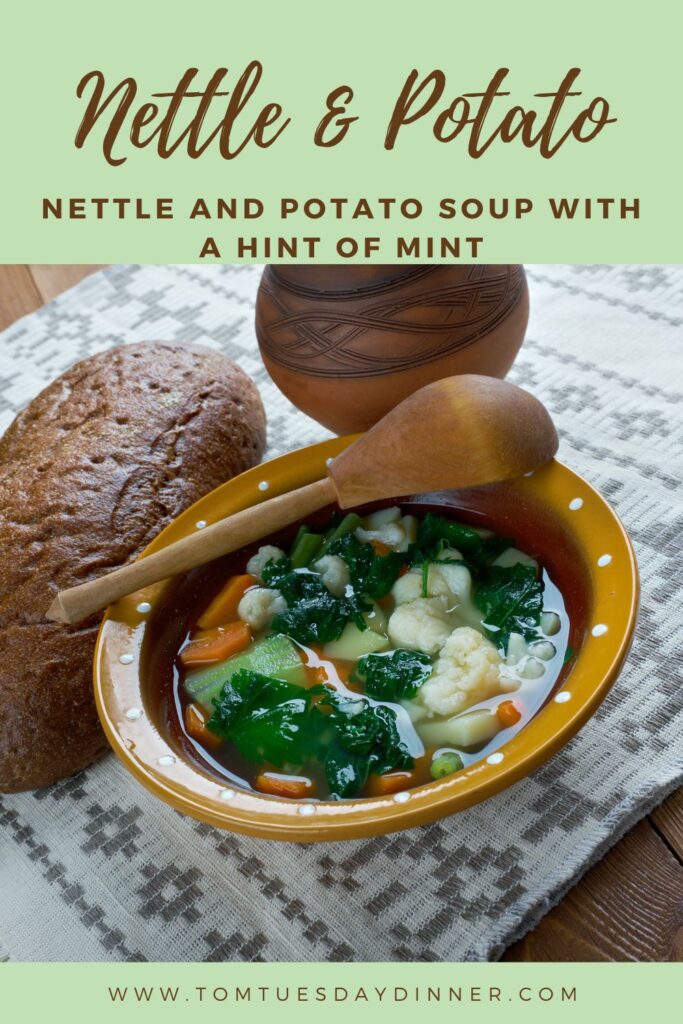 A bowl of nettle and potato soup with a hint of mint, accompanied by a loaf of bread and a wooden spoon, placed on a patterned cloth.