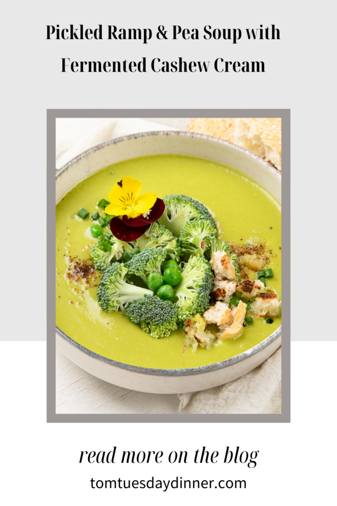 A bowl of Pickled Ramp & Pea Soup with Fermented Cashew Cream, garnished with broccoli, peas, croutons, and edible flowers.